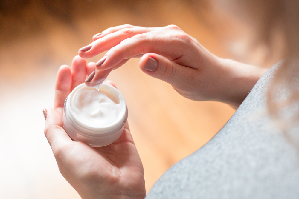 Person's hand holding a small container of lotion.